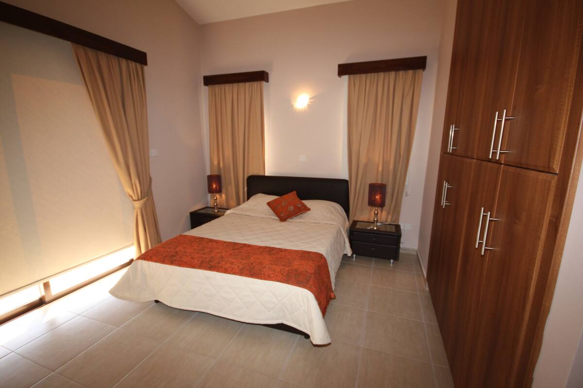 Una habitación de hotel con cama, mesitas de noche, un armario y cortinas.