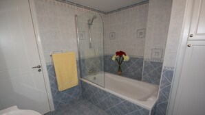 Un baño con ducha acristalada, bañera blanca y toalla amarilla colgada en la pared.