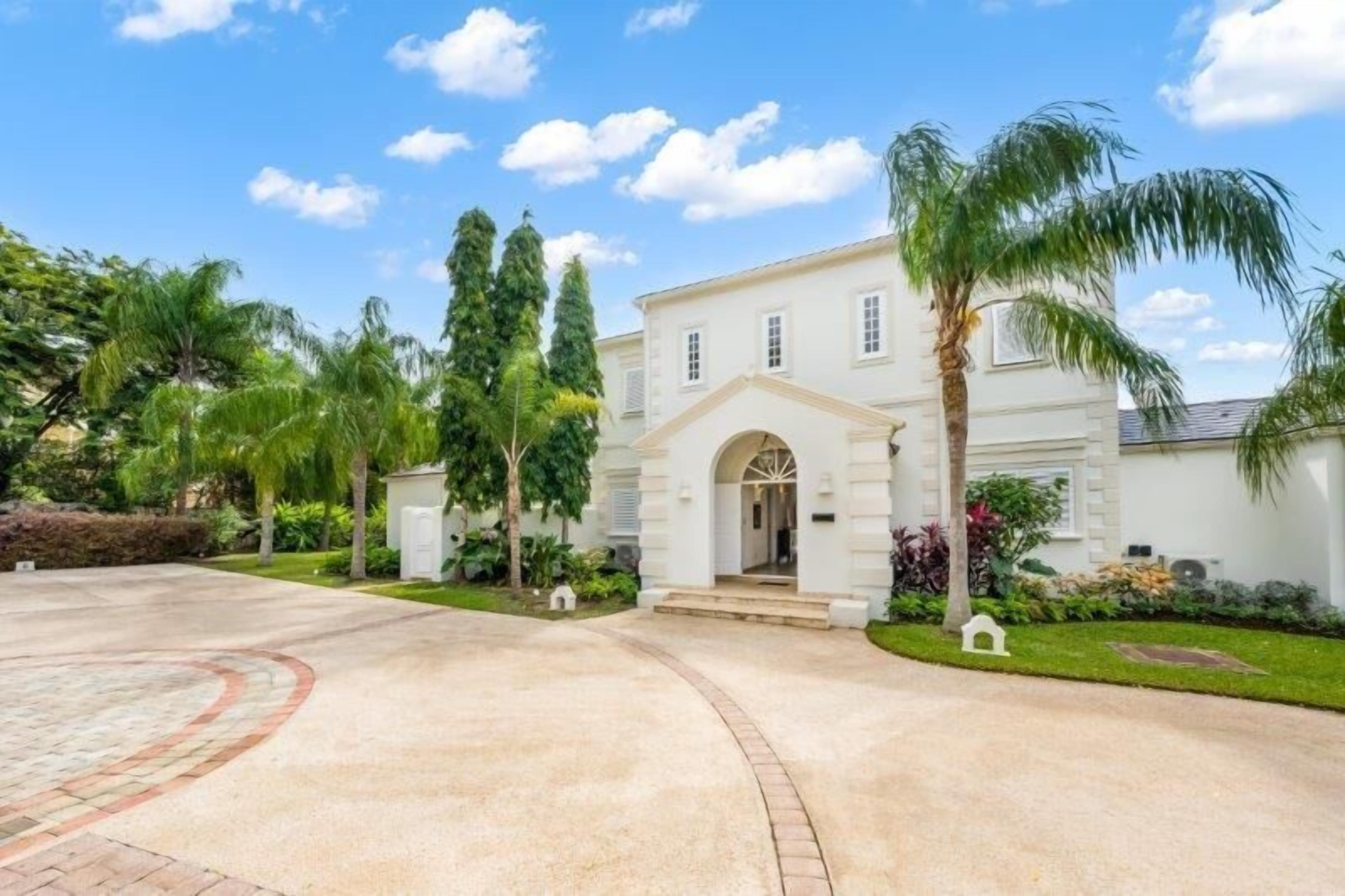 A two-story house with a central entrance, surrounded by a well-maintained lawn and palm trees.
