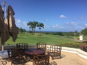 A patio with a round table and chairs, overlooking a golf course with palm trees and a view of the ocean. - Royal Westmoreland Mahogany Drive by Island Villas (Westmoreland)