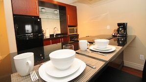A modern kitchen with a black refrigerator, microwave, and coffee maker. There are white bowls and plates on a glass table.