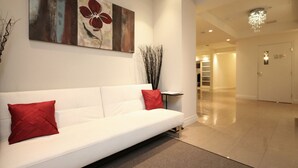 A modern lobby with a white sofa, red cushions, a large abstract painting, and a tall vase with branches.