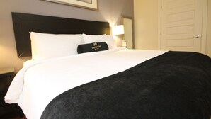 A hotel room with a large bed, a headboard, a nightstand, a lamp, a door, and a framed picture on the wall.