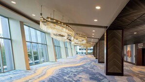 A hotel corridor with large windows, a patterned carpet, and multiple chandeliers.