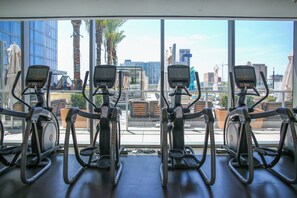 Four stationary bikes in a gym with large windows overlooking a cityscape.