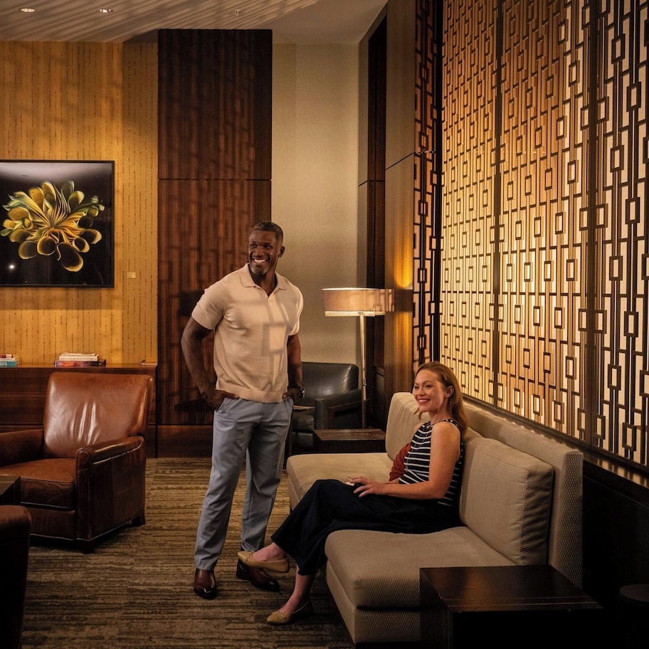 A modern hotel lobby with leather seating, a large abstract painting, and a decorative wall panel.