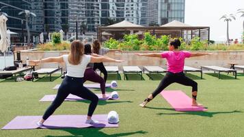 A group of people practicing yoga outdoors on a grassy area with a modern building in the background.
