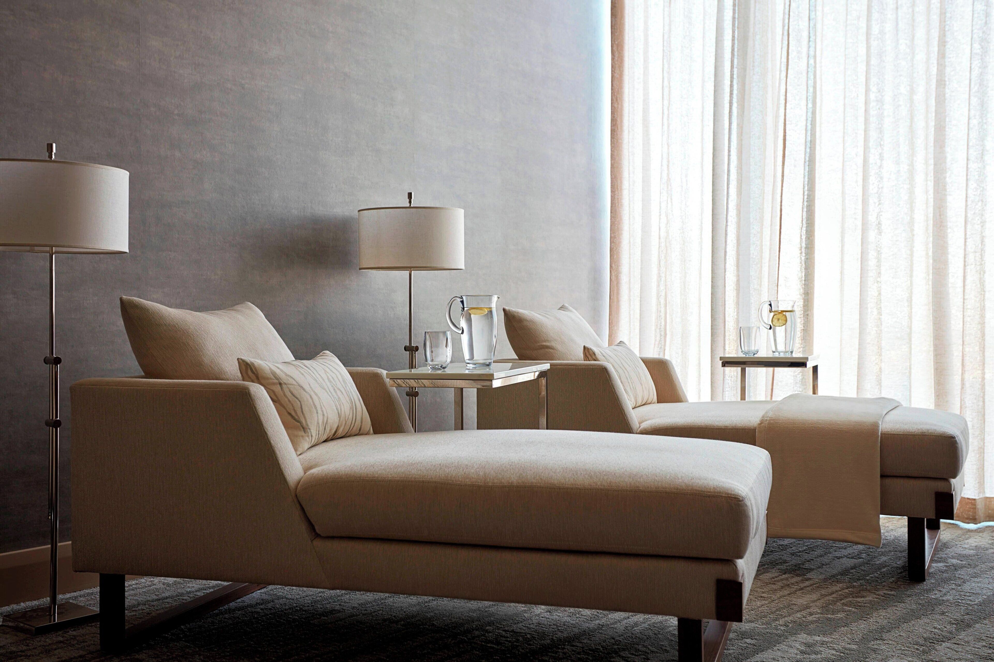 A hotel room with a sofa set, two side tables, a floor lamp, and a window with curtains.