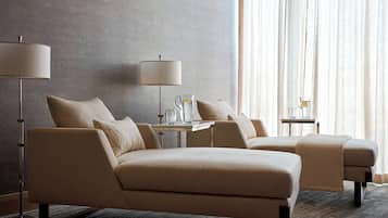 A hotel room with a sofa set, two side tables, a floor lamp, and a window with curtains.
