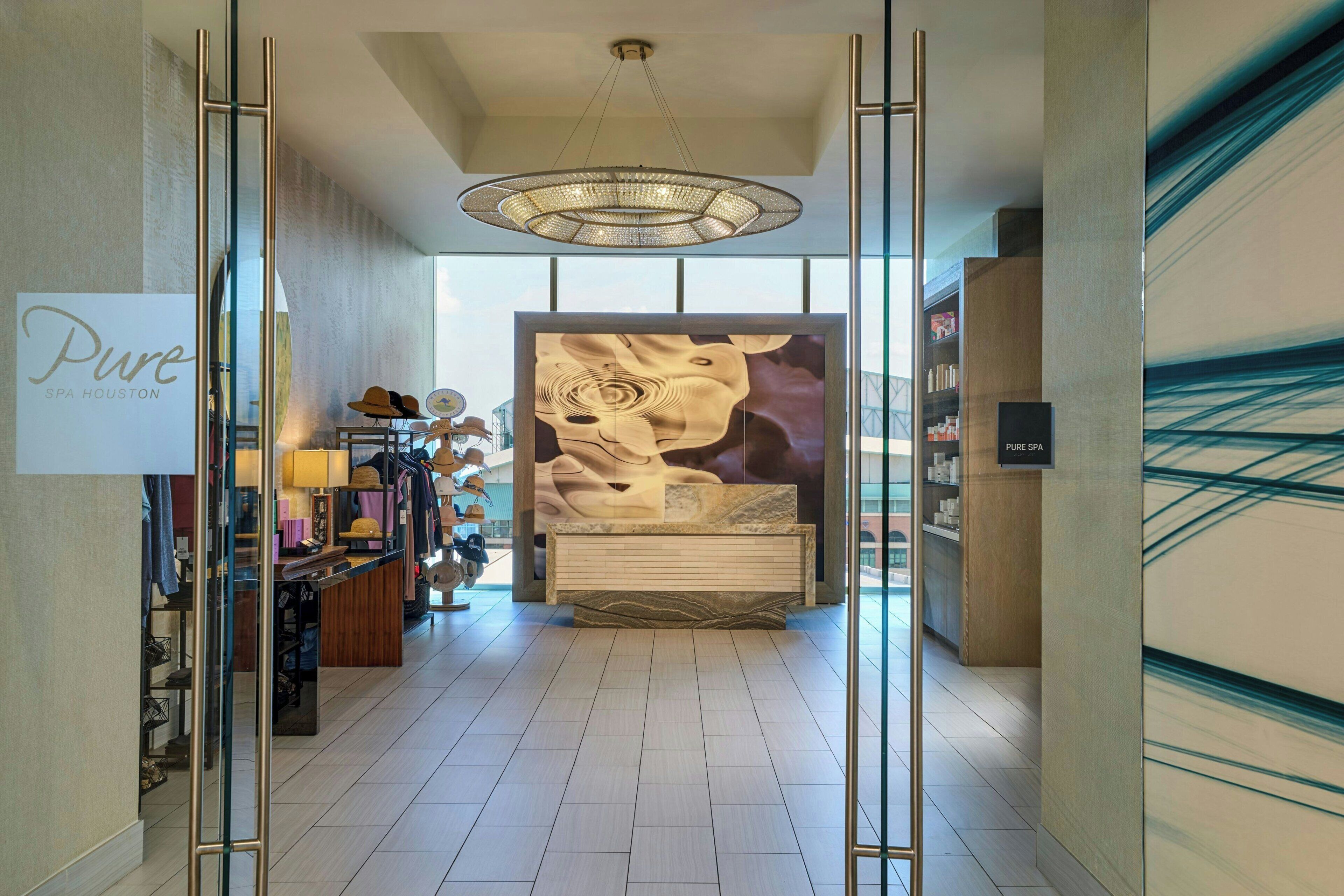 A modern spa interior with a reception desk, a chandelier, and a large abstract mural.