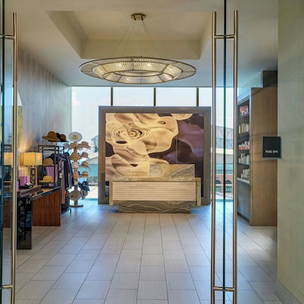 A modern spa interior with a reception desk, a chandelier, and a large abstract mural.
