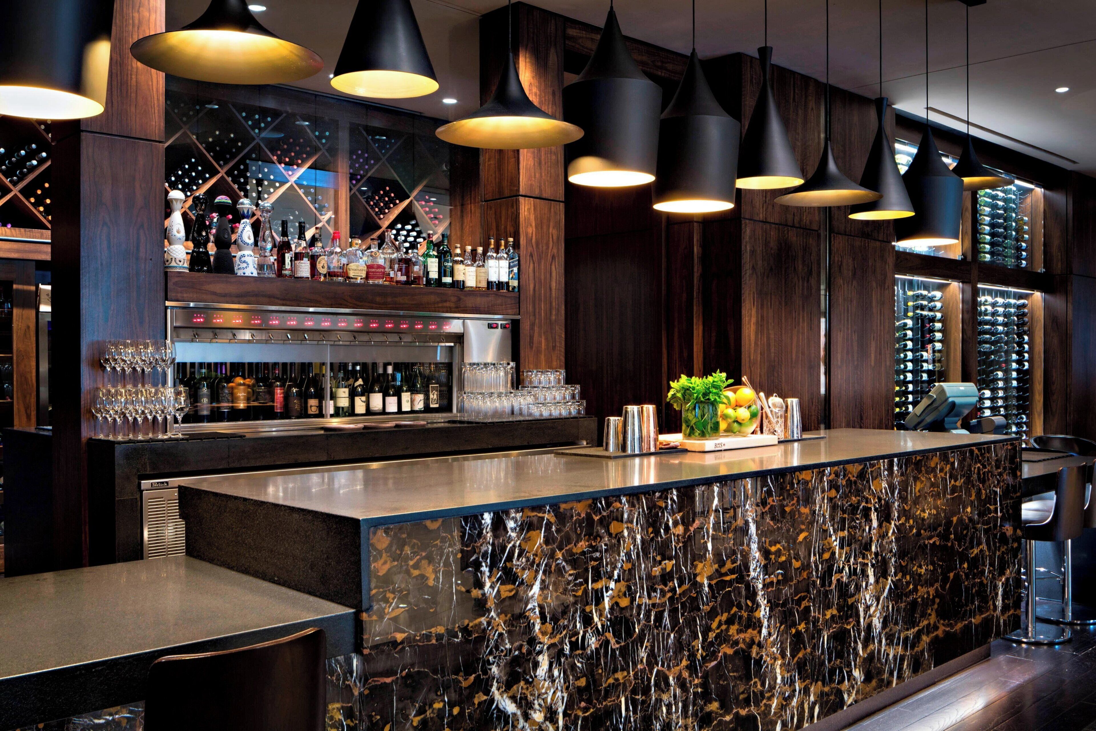 A bar area with a marble countertop, hanging pendant lights, and a wine rack in the background.