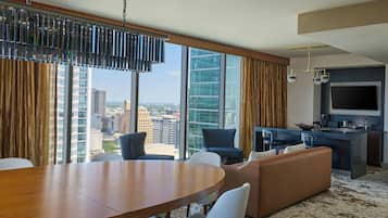 Quarto de hotel moderno com área de refeições, assentos, cozinha e uma grande janela com vista para a cidade.