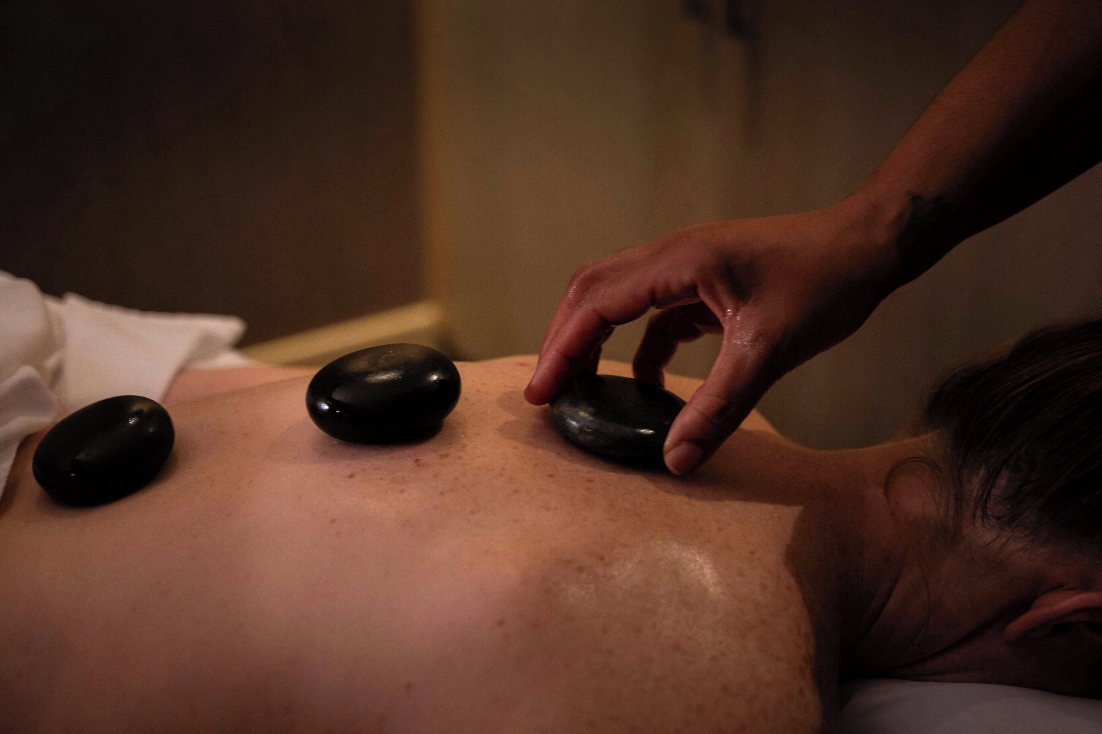 A person receiving a massage with black stones on their back.