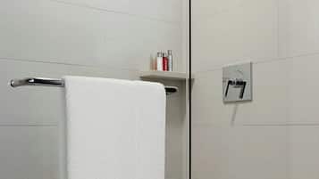 Un baño moderno con cabina de ducha de vidrio, una toalla blanca colgada en un perchero metálico y un estante pequeño con artículos de aseo.