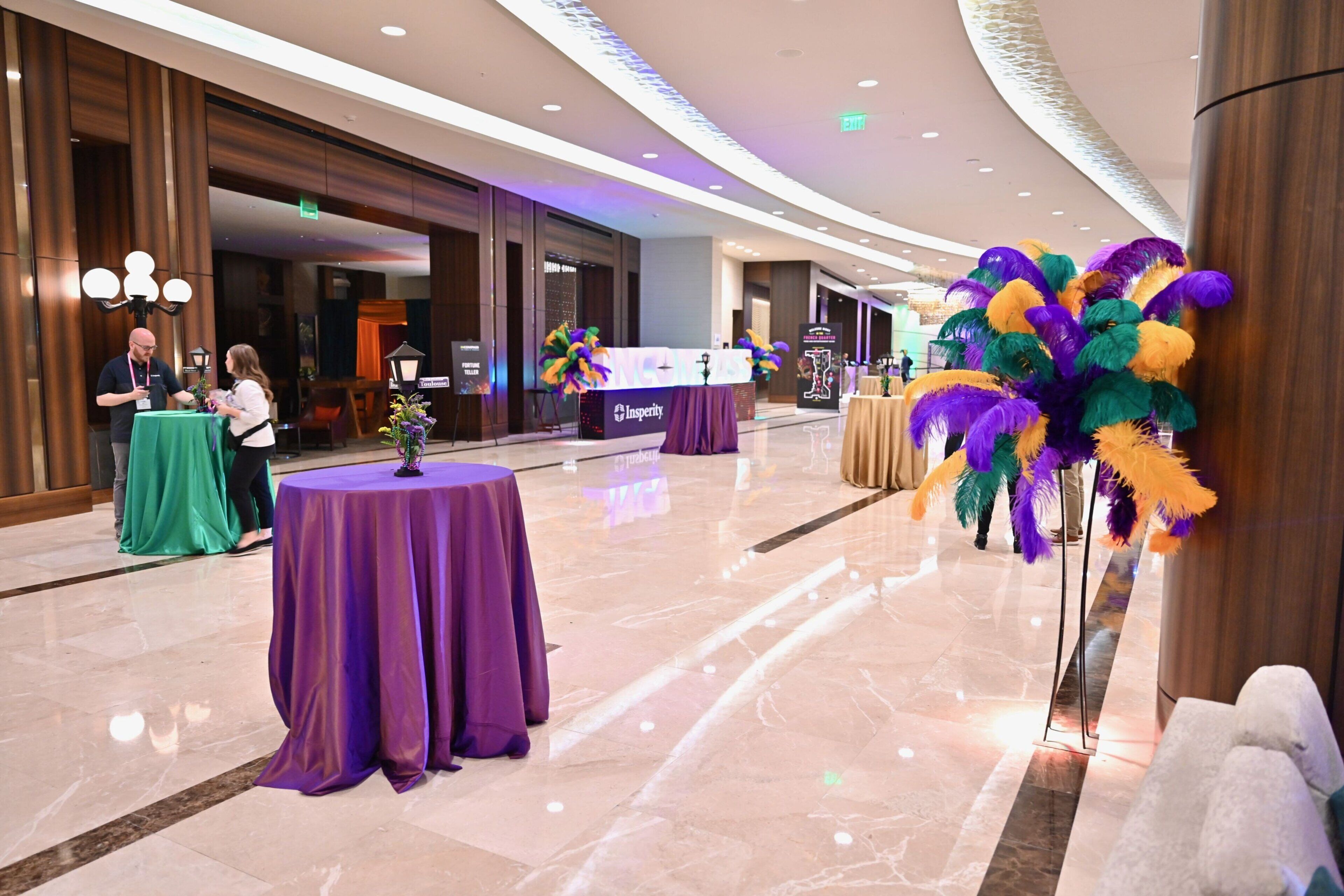 A hotel lobby with marble flooring, purple tablecloths, and a large decorative floral arrangement.