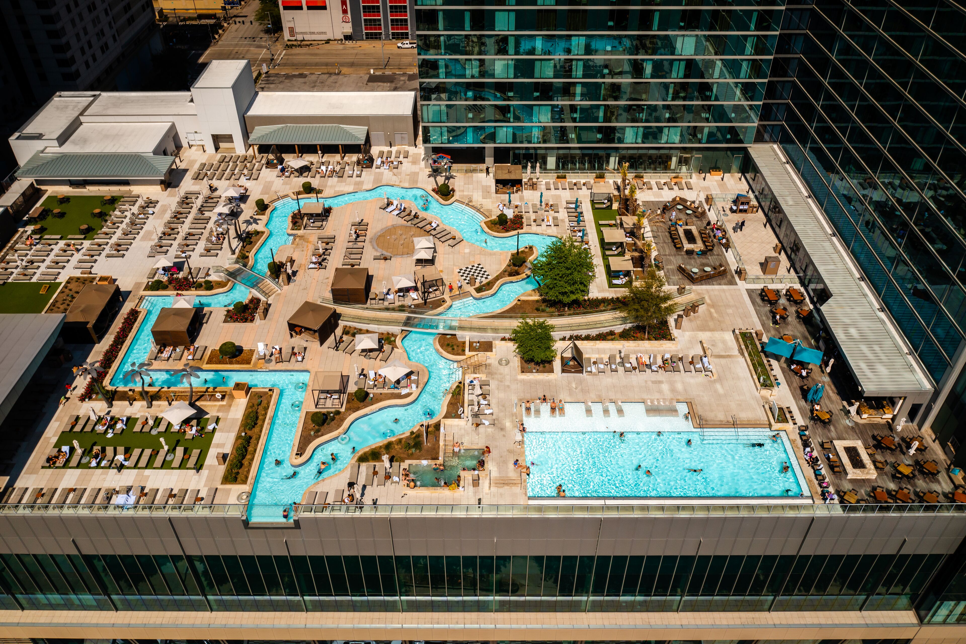 A rooftop pool area with multiple swimming pools, lounge chairs, and sunbeds.