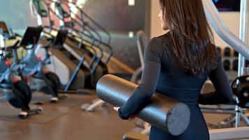 A gym with exercise equipment and a person holding a yoga mat.