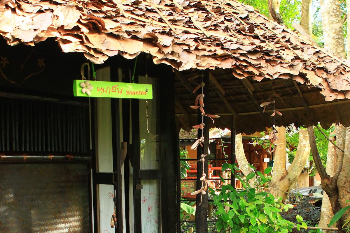 A rustic wooden structure with a thatched roof, a bench with cushions, and a potted plant.