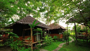 A rustic wooden structure with a thatched roof, surrounded by lush greenery and a stone pathway.