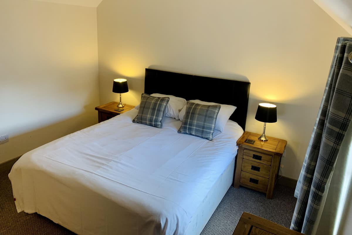 A neatly made bed with white linens, two plaid pillows, and two bedside tables with lamps.