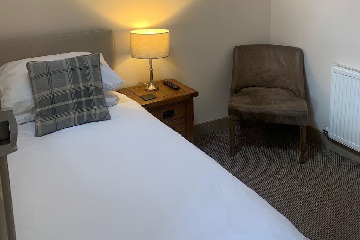 A hotel room with a bed, a nightstand with a lamp, a chair, and a radiator.