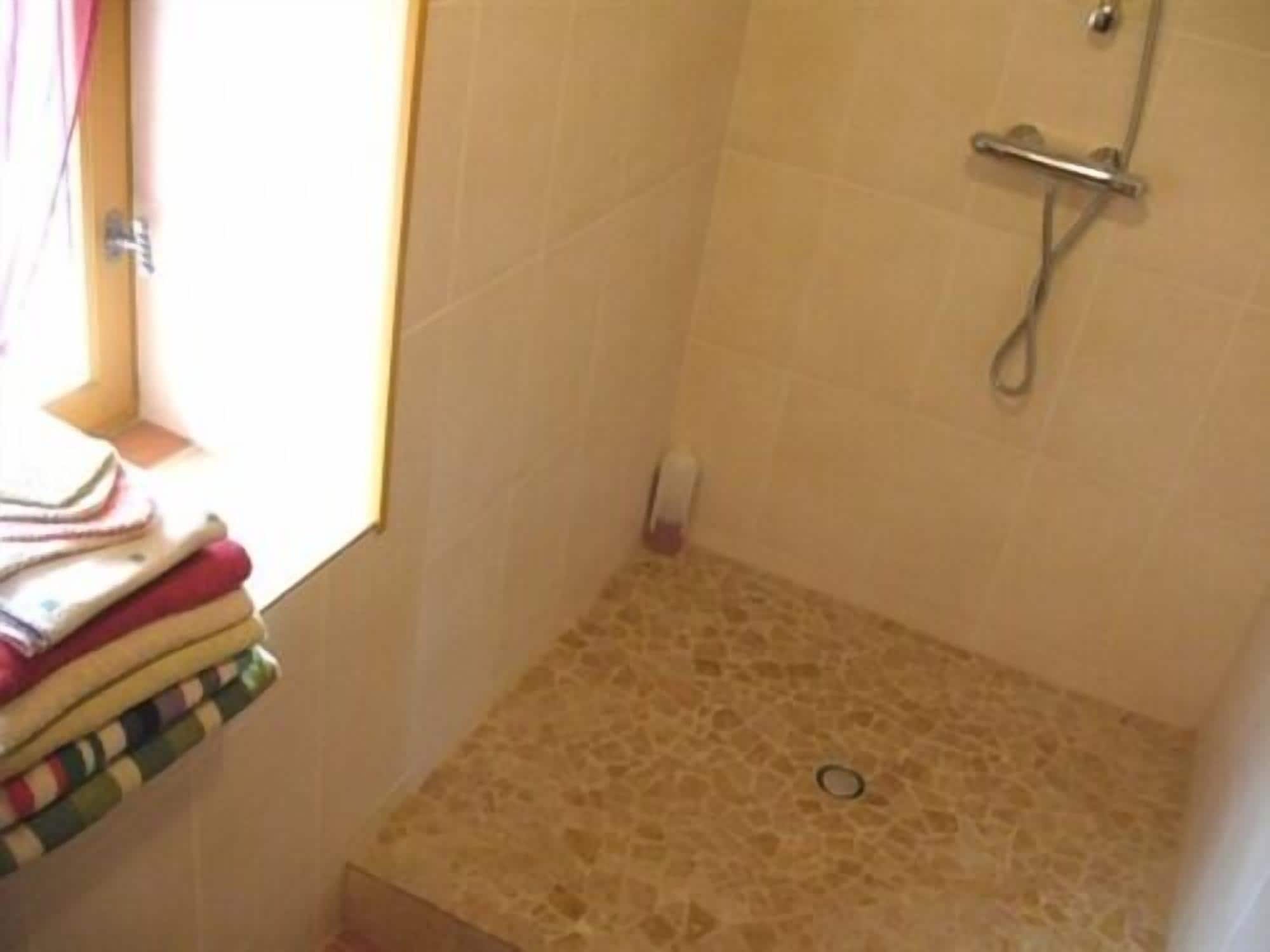 Une petite salle de bain avec une douche, une fenêtre avec des rideaux et un sol carrelé.