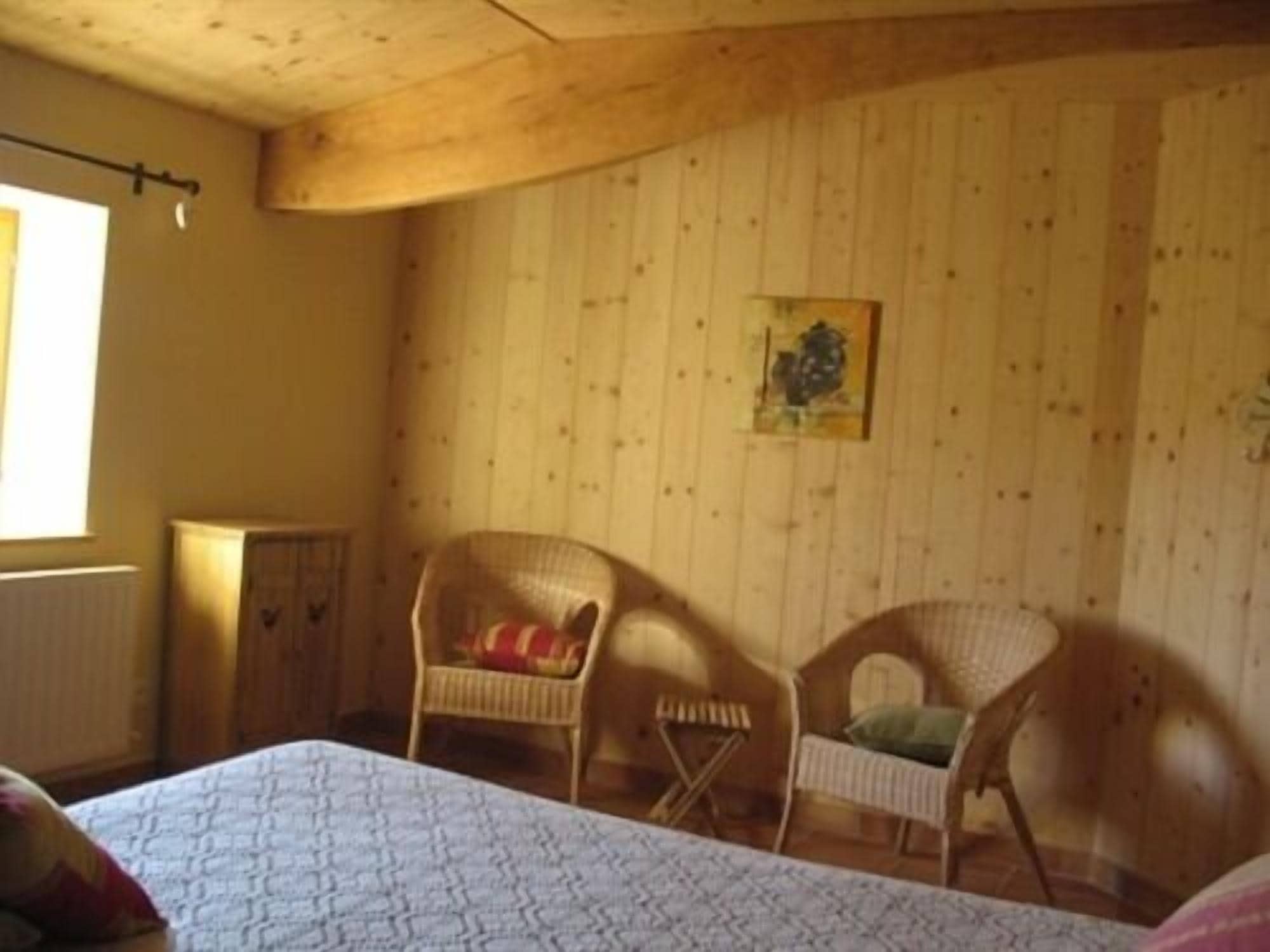 Una habitación con una cama, dos sillas de mimbre, un radiador y un cuadro en la pared.