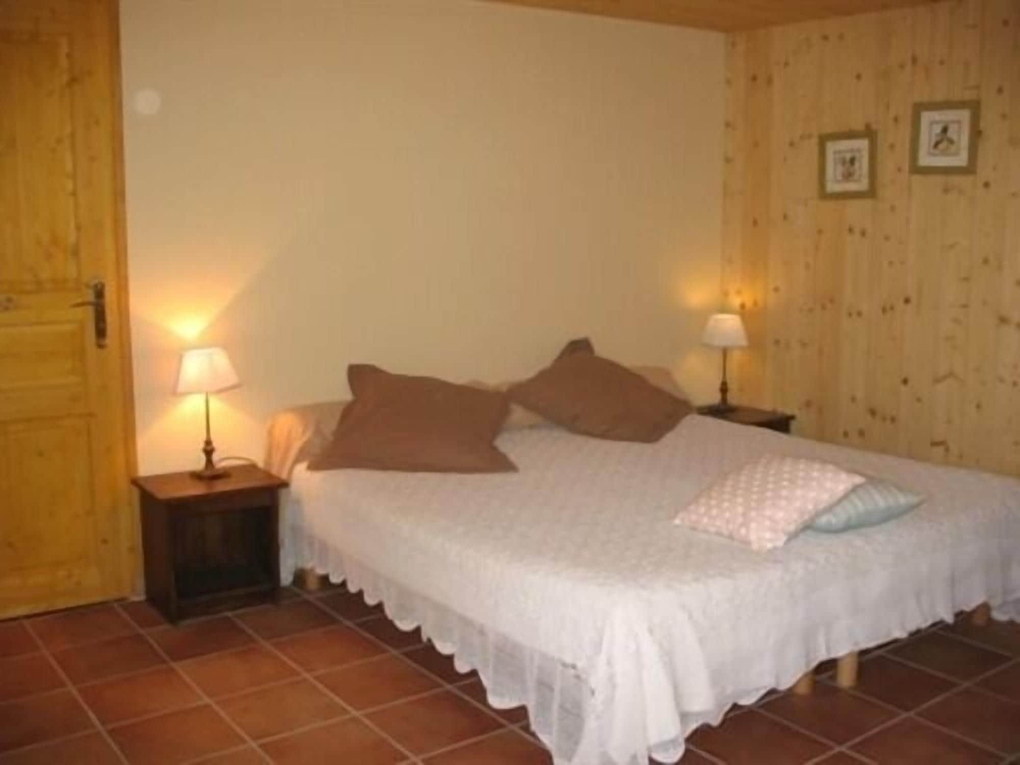 A bedroom with a bed, two bedside tables with lamps, a wooden door, and a tiled floor.