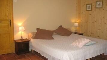 A bedroom with a bed, two bedside tables with lamps, a wooden door, and a tiled floor.