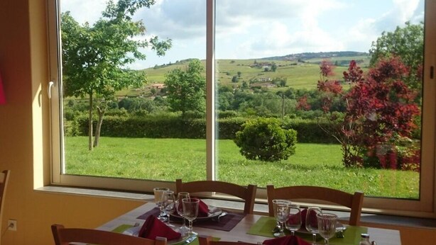 Une table à manger dressée pour quatre personnes, avec une vue imprenable sur des collines verdoyantes et des arbres, visible à travers une grande fenêtre.