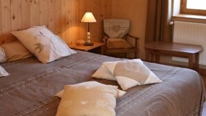 Une pièce aux murs lambrissés, contenant un lit, une chaise, une table et une lampe.