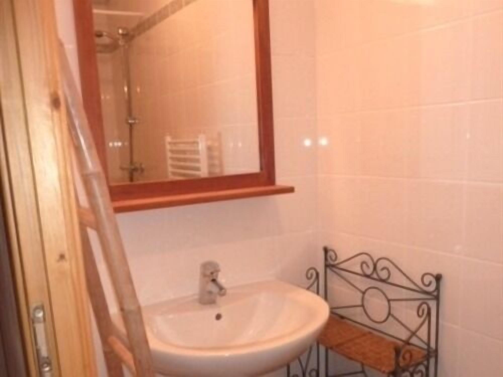 A bathroom with a white sink, a mirror with a wooden frame, and a metal shelf.