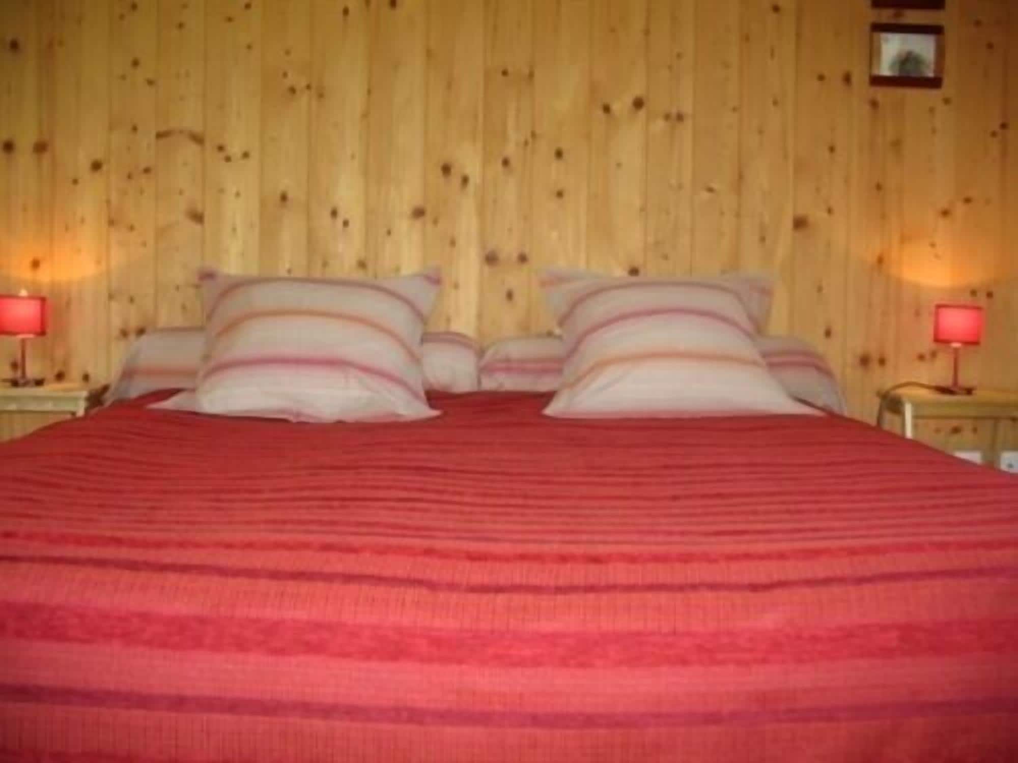 Un letto con una coperta rossa, due comodini con lampade e pareti in legno.