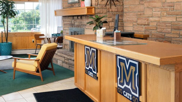 A reception area with a stone wall, wooden ceiling beams, and a counter with a logo. - The Sapphire Motel (Bozeman)