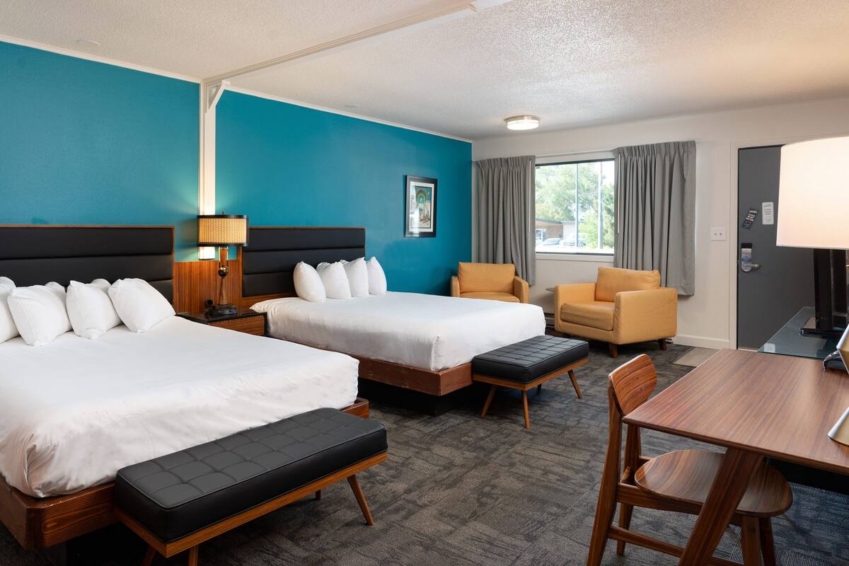 A hotel room with two beds, a desk, and a chair.