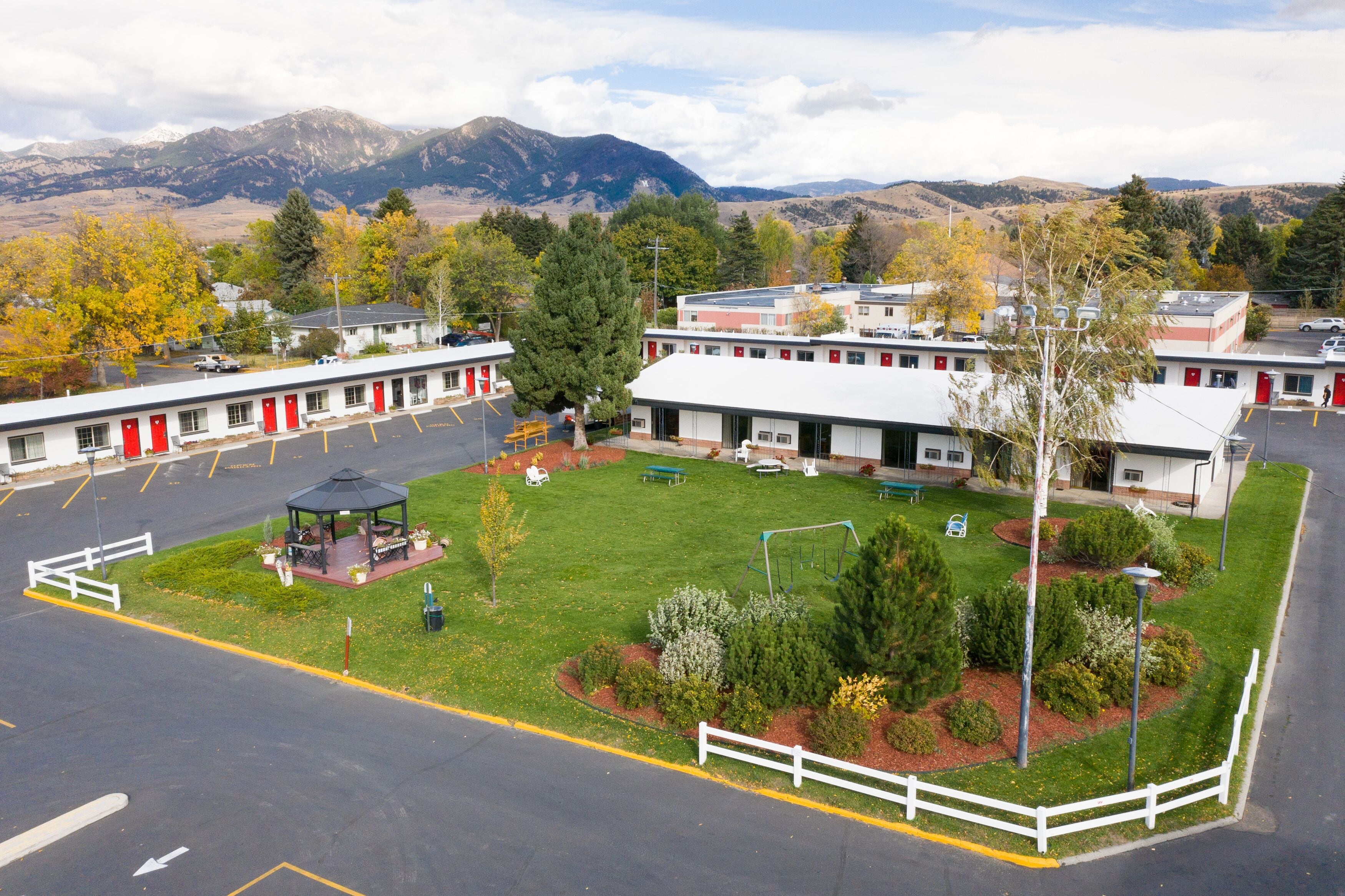 Un motel con patio central, varias habitaciones con puertas rojas y montañas al fondo.