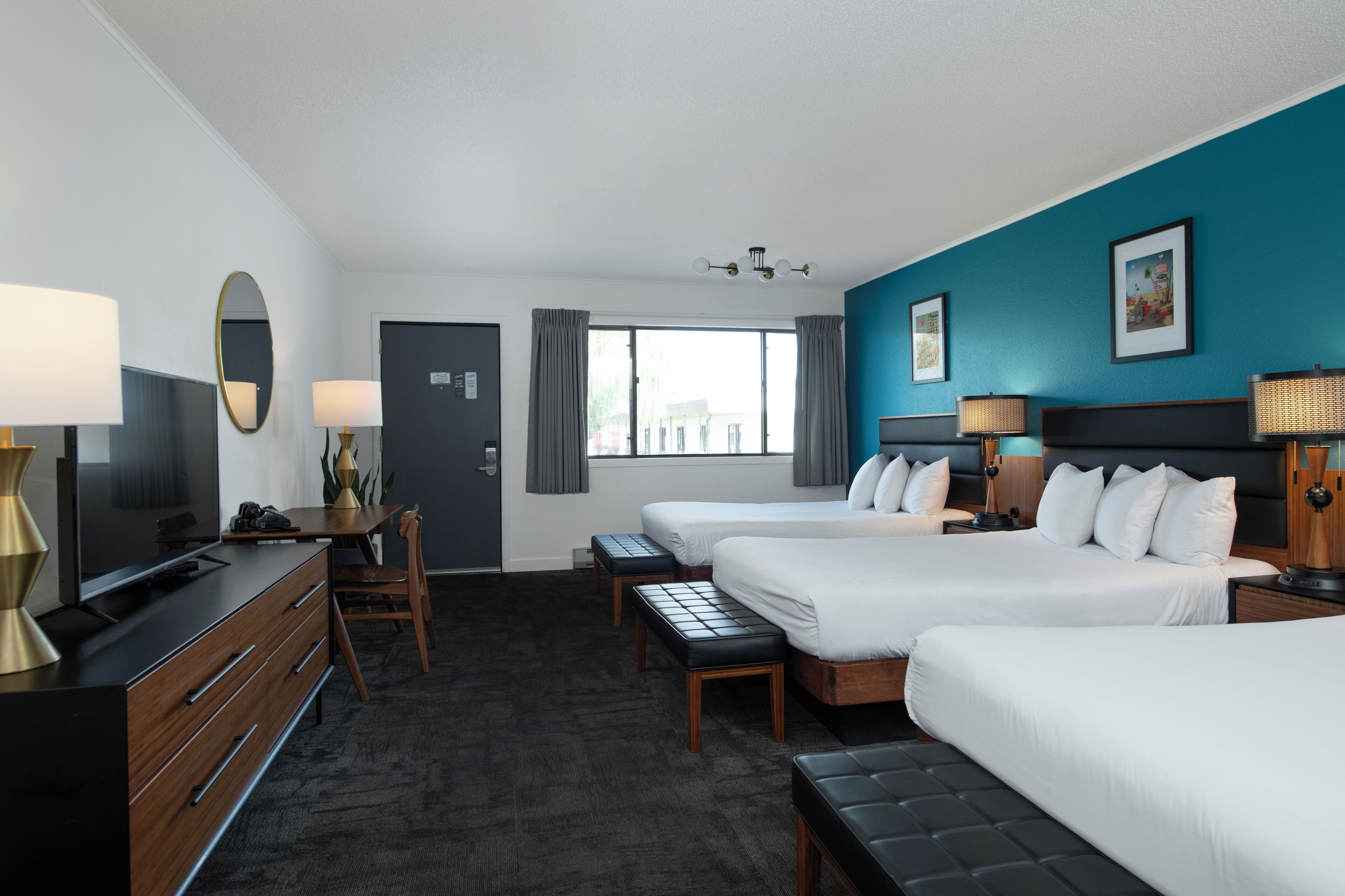 A hotel room with two beds, a desk, a TV, and a window with curtains.
