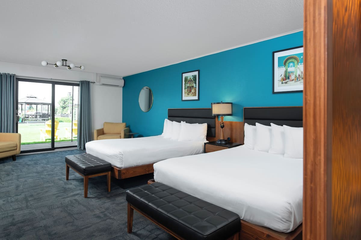 A hotel room with two beds, a large window, a sofa, and a view of the outdoors.