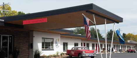 A motel with a 6" clearance sign, American flags, and a vintage red car parked in front.