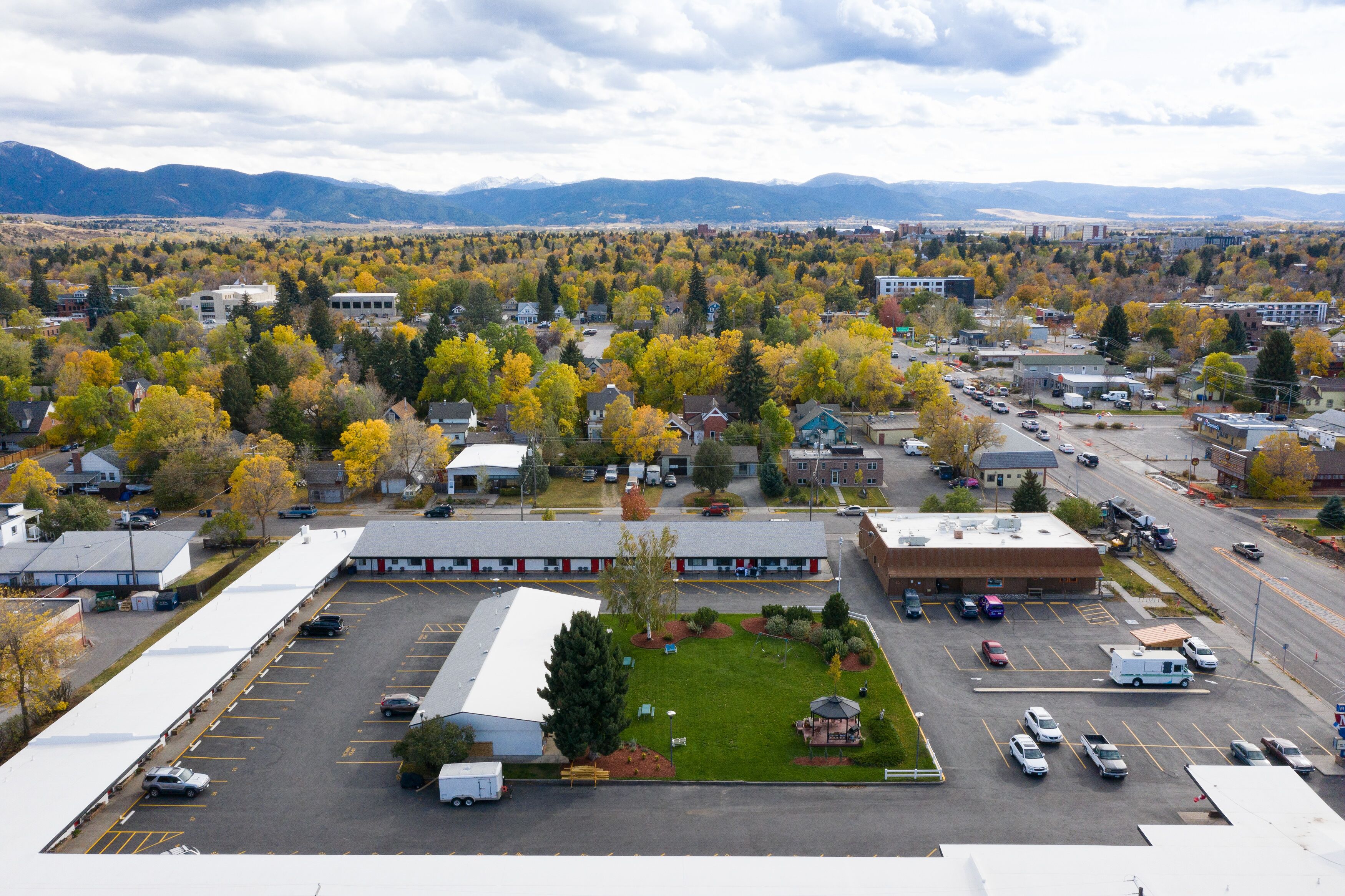 A parking lot with several buildings, a grassy area, and a mountainous background.
