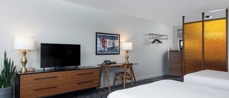 Een hotelkamer met een bed, een bureau met stoel, een televisie en een potplant.