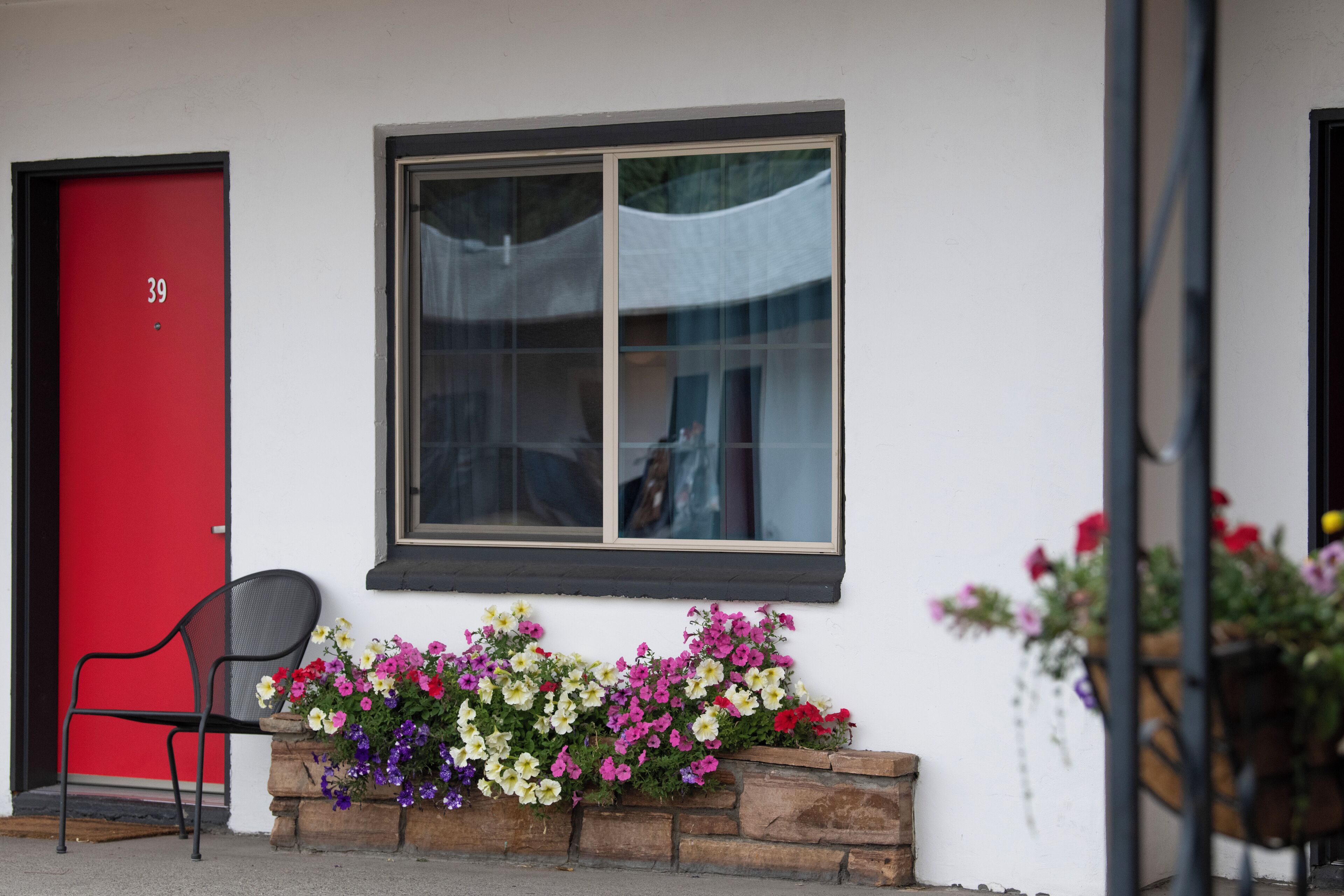 A red door with the number 39, a window with a white curtain, and a planter with colorful flowers.