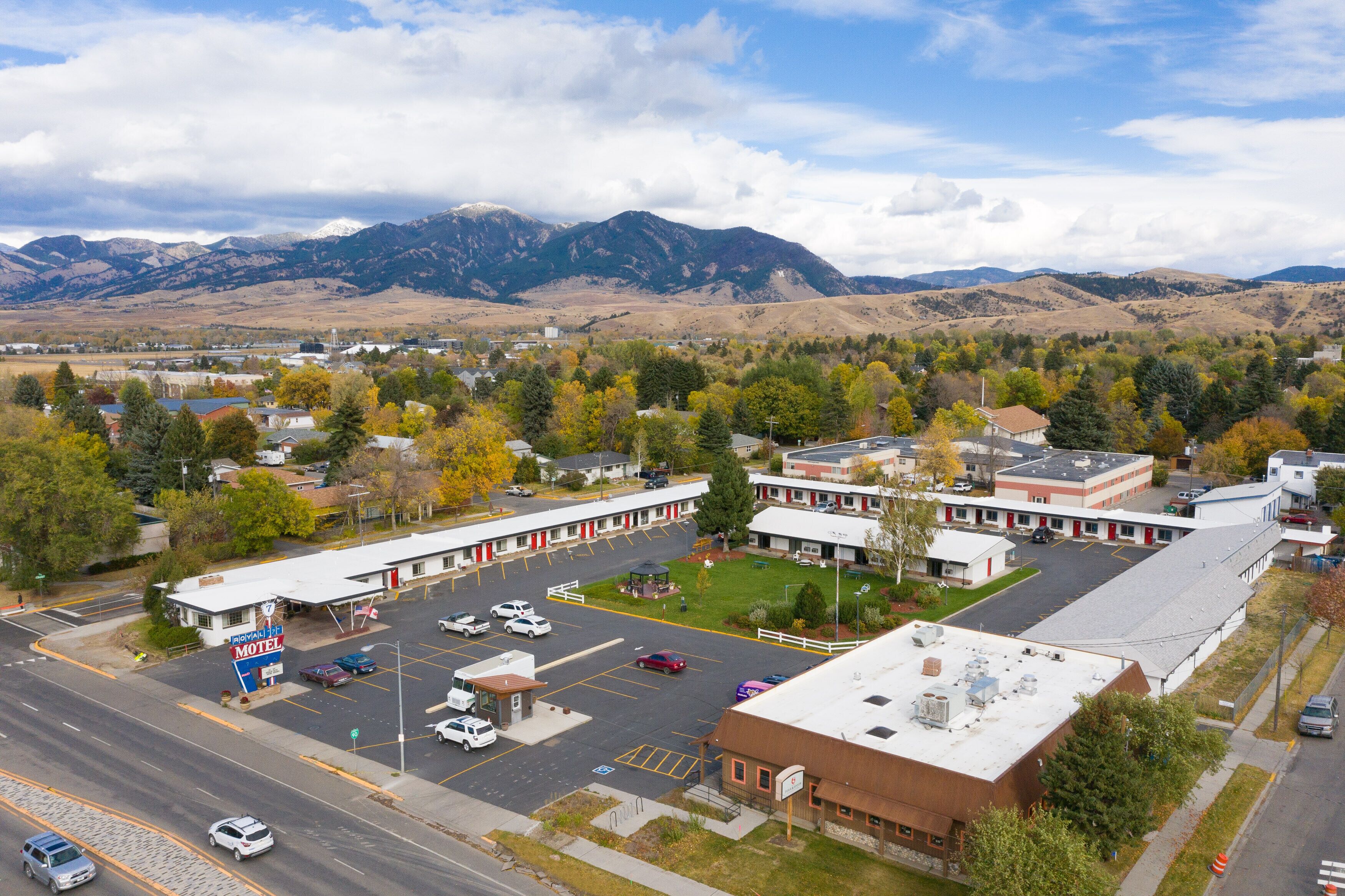A motel with a parking lot, a small garden, and a mountain backdrop.