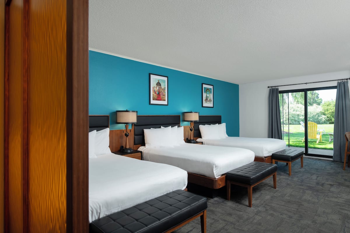 A hotel room with three beds, a large window, and a view of the outdoors.