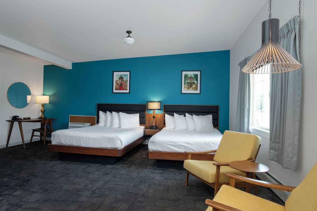 A hotel room with two beds, a desk, a chair, and a hanging light fixture.