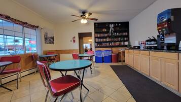 A restaurant with a bar area, seating with red chairs, a ceiling fan, and a bookshelf with various items.