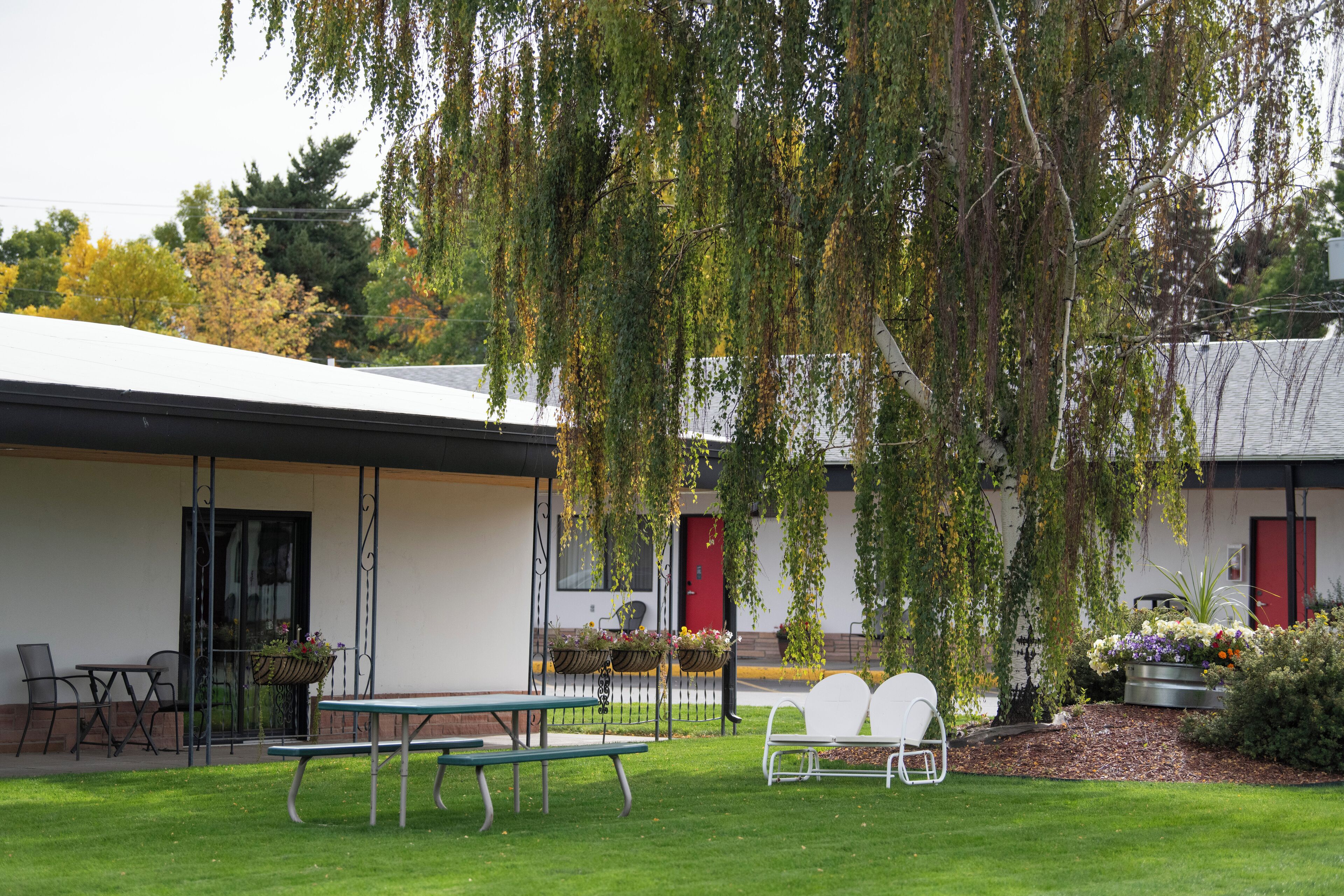 A patio area with a table and chairs, a hanging plant, and a building with a red door in the background.