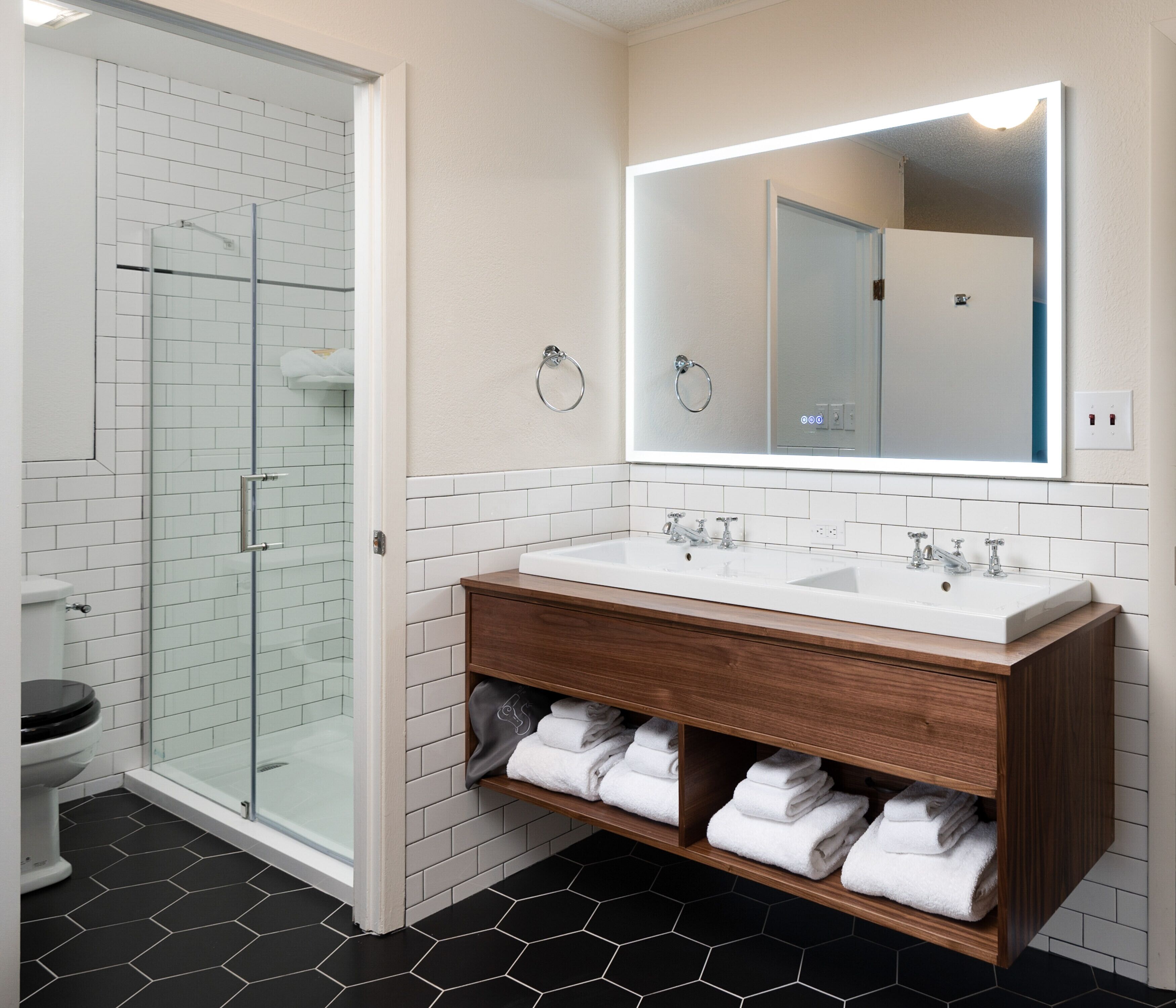 A bathroom with a glass shower enclosure, a double sink vanity, and a large mirror.