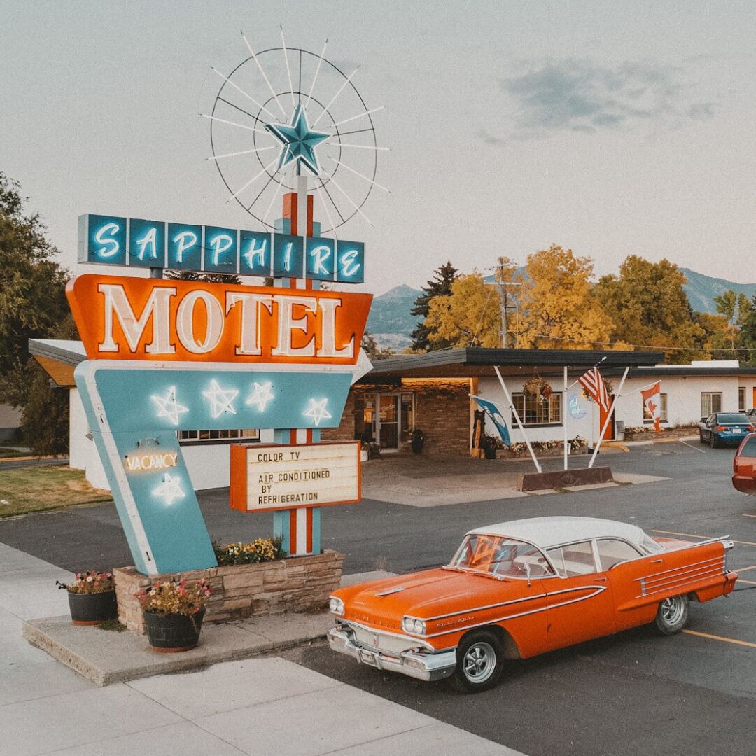 A vintage motel sign with a star and windmill, a vintage car parked in front, and a building with a sign that reads "Sapphire Motel".